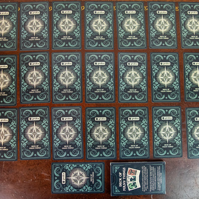 Photo of the backs of the cards featuring the words "gmdice" and "Deck of Many Things" on a black background with a white star in the middle and green swirl designs on the sides.