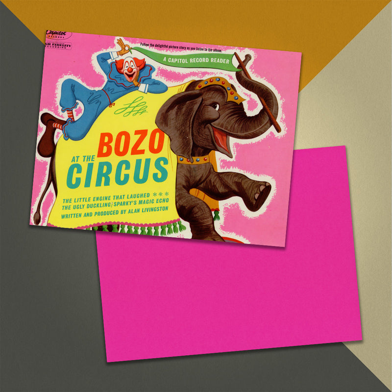 Photo of a 11” x 8.5” notebook cover made from an upcycled Pinto Colvig, Billy May “Bozo At The Circus” album sleeve and the back cover with hot pink cardstock on an orange, cream and grey background.