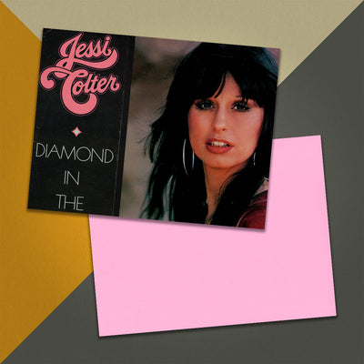 Photo of a 11” x 8.5” notebook cover made from an upcycled Jessi Colter “Diamond in the Rough” album sleeve and the back cover with pink cardstock on an orange, cream and grey background.