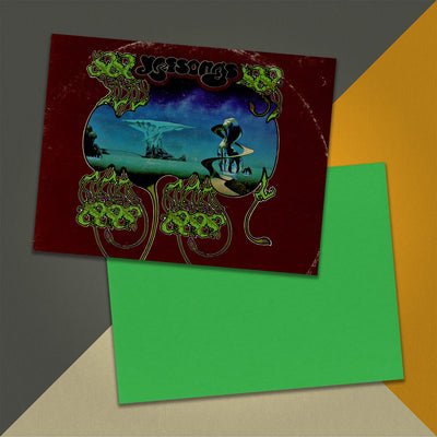 Photo of a 11” x 8.5” notebook cover made from an upcycled Yes “Yessongs” album sleeve and the back cover with green cardstock on an orange, cream and grey background.