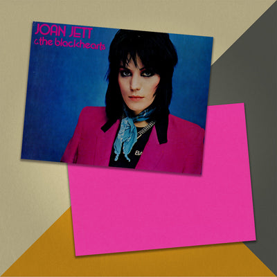 Photo of a 11” x 8.5” notebook cover made from an upcycled Joan Jett & the Blackhearts “I Love Rock ‘N Roll” album sleeve and the back cover with hot pink cardstock on an orange, cream and grey background.