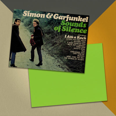 Photo of a 11” x 8.5” notebook cover made from an upcycled Simon & Garfunkel “Sounds of Silence” album sleeve and the back cover with lime green cardstock on an orange, cream and grey background.