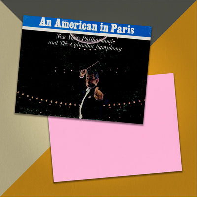 Photo of a 11” x 8.5” notebook cover made from an upcycled Gershwin, Leonard Bernstein “Rhapsody In Blue / An American In Paris” album sleeve and the back cover with pink cardstock on an orange, cream and grey background.