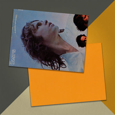 Photo of a 11” x 8.5” notebook cover made from an upcycled The Doors “13” album sleeve and the back cover with orange cardstock on an orange, cream and grey background.