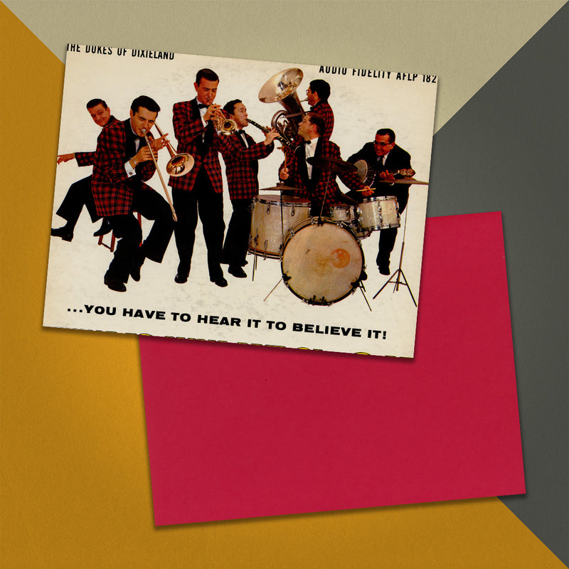 Photo of a 11” x 8.5” notebook cover made from an upcycled The Dukes Of Dixieland “You Have To Hear It To Believe It!” album sleeve and the back cover with red cardstock on an orange, cream and grey background.