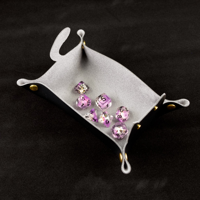 Photo of a black cat shaped dice tray from above with a set of dice inside on a black background.