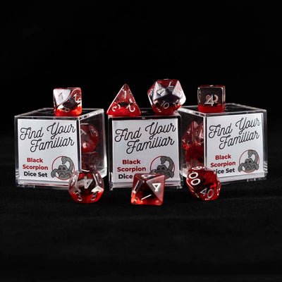 A set of clear and red polyhedral dice with black scorpion inclusions sitting on top and around a three small acrylic boxes with the words "Find Your Familiar" and "Black Scorpion Dice Set" on a black background.