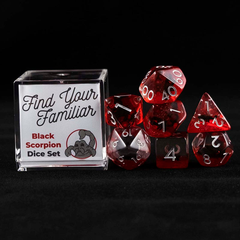 A set of clear and red polyhedral dice with black scorpion inclusions sitting to the right of a small acrylic box with the words "Find Your Familiar" and "Black Scorpion Dice Set" on a black background.