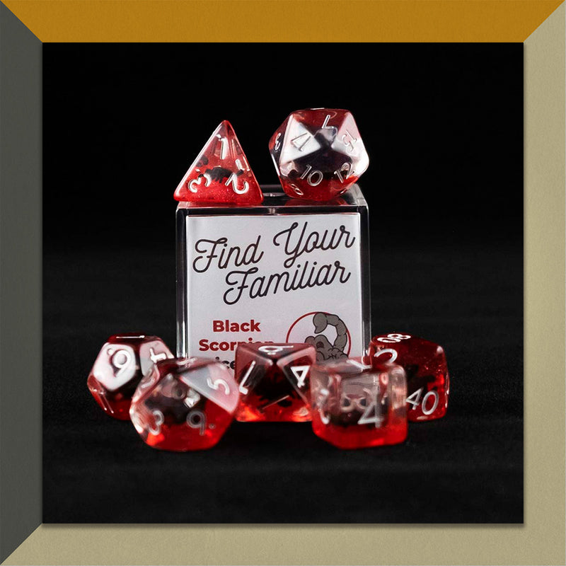 A set of clear and red polyhedral dice with black scorpion inclusions sitting on top and around a small acrylic box with the words "Find Your Familiar" and "Black Scorpion Dice Set" on an orange, cream and grey background.