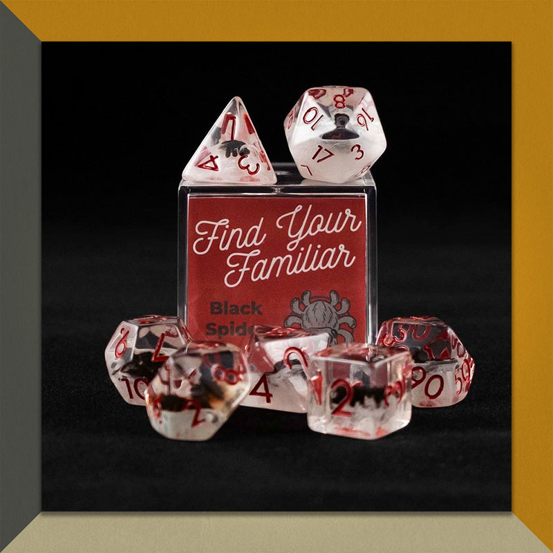 A set of clear and cloudy polyhedral dice with black spider inclusions sitting on top and around a small acrylic box with the words "Find Your Familiar" and "Black Spider Dice Set" on an orange, cream and grey background.