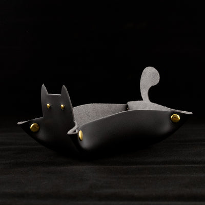 Photo of a black cat shaped dice tray facing left on a black background.