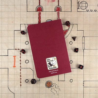 The dark red back cover of the blood hunter notebook with "The Raven and the Goose" logo on the bottom. The notebook sits on a grid map surrounded by dice.