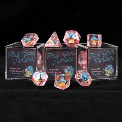 A set of pink polyhedral dice with blue and pink cap mushroom inclusions sitting on top and around a three small acrylic boxes with the words "Find Your Familiar" and "Oops, It's Mushrooms Dice Set" on a black background.