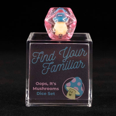 A 20 sided pink die with blue and pink cap mushroom inclusions sitting on top of a small acrylic box with the words "Find Your Familiar" and "Oops, It's Mushrooms Dice Set" on a black background.