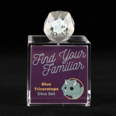 A 20 sided clear die with blue triceratops inclusions sitting on top of a small acrylic box with the words "Find Your Familiar" and "Blue Triceratops Dice Set" on a black background.