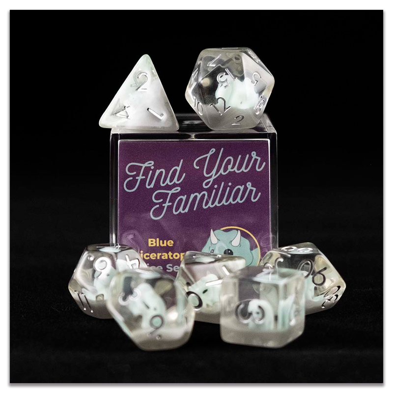 A set of clear polyhedral dice with blue triceratops inclusions sitting on top and around a small acrylic box with the words "Find Your Familiar" and "Blue Triceratops Dice Set" on a transparent background.