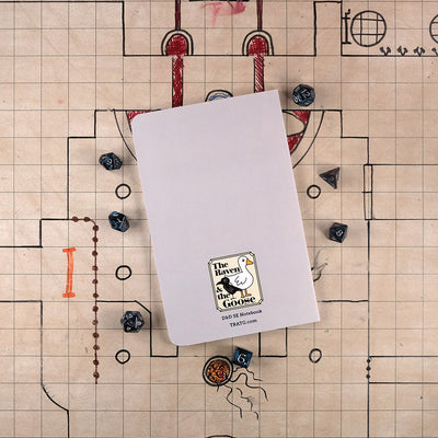 The light gray back cover of the fighter notebook with "The Raven and the Goose" logo on the bottom. The notebook sits on a grid map surrounded by dice.