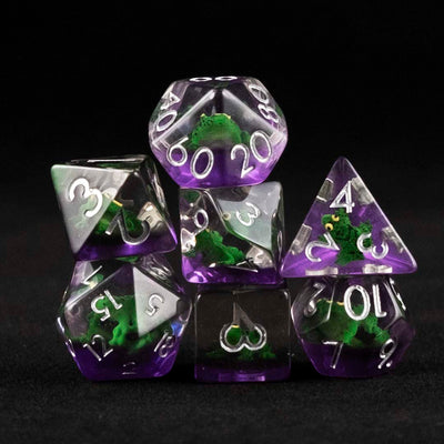 A set of clear and purple polyhedral dice with green frog inclusions on a black background.