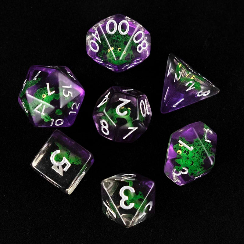 A set of clear and purple polyhedral dice with green frog inclusions from above on a black background.