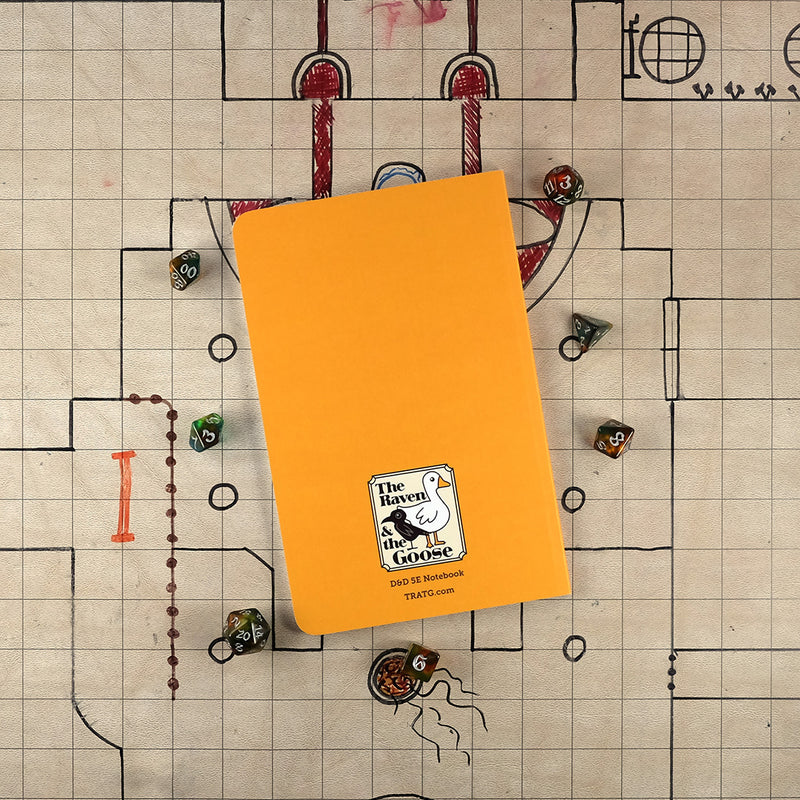 The orange back cover of the paladin notebook with "The Raven and the Goose" logo on the bottom. The notebook sits on a grid map surrounded by dice.