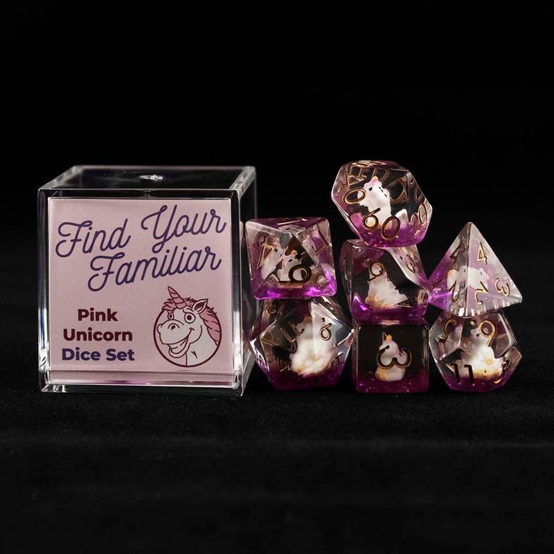 A set of clear and purple polyhedral dice with pink unicorn inclusions sitting to the right of a small acrylic box with the words "Find Your Familiar" and "Pink Unicorn Dice Set" on a black background.