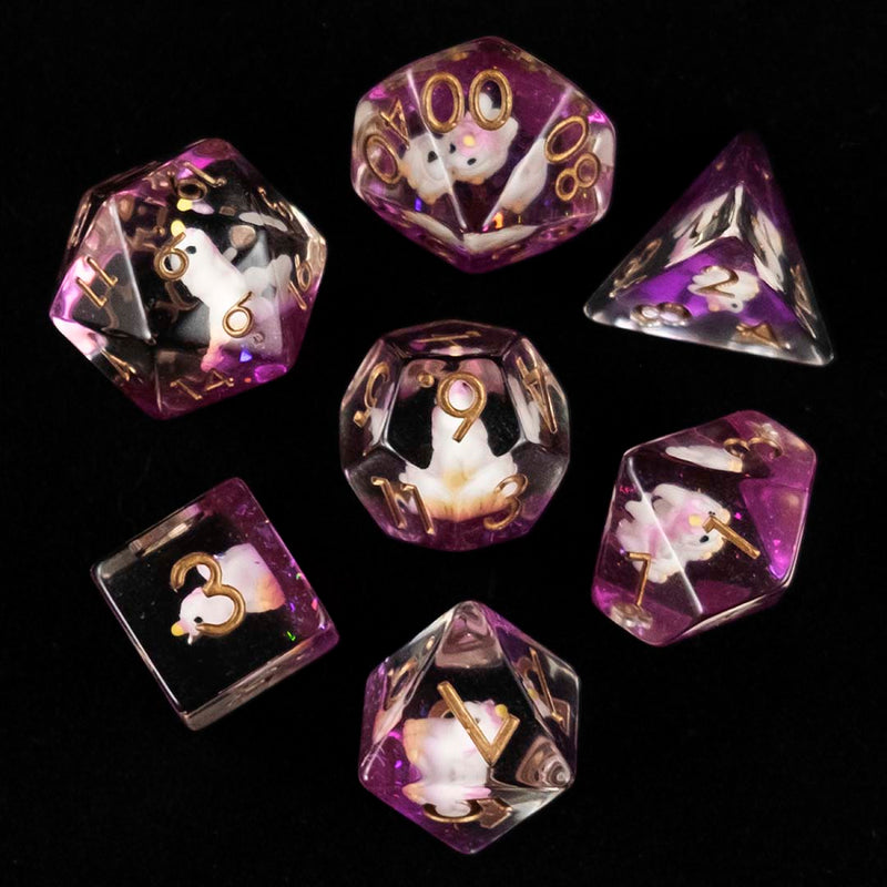 A set of clear and purple polyhedral dice with pink unicorn inclusions from above on a black background.