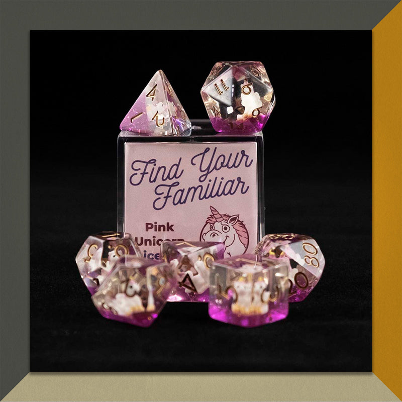 A set of clear and purple polyhedral dice with pink unicorn inclusions sitting on top and around a small acrylic box with the words "Find Your Familiar" and "Pink Unicorn Dice Set" on an orange, cream and grey background.