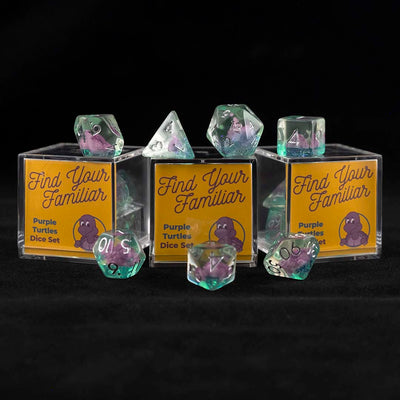 A set of clear green polyhedral dice with purple turtle inclusions sitting on top and around a three small acrylic boxes with the words "Find Your Familiar" and "Purple Turtles Dice Set" on a black background.