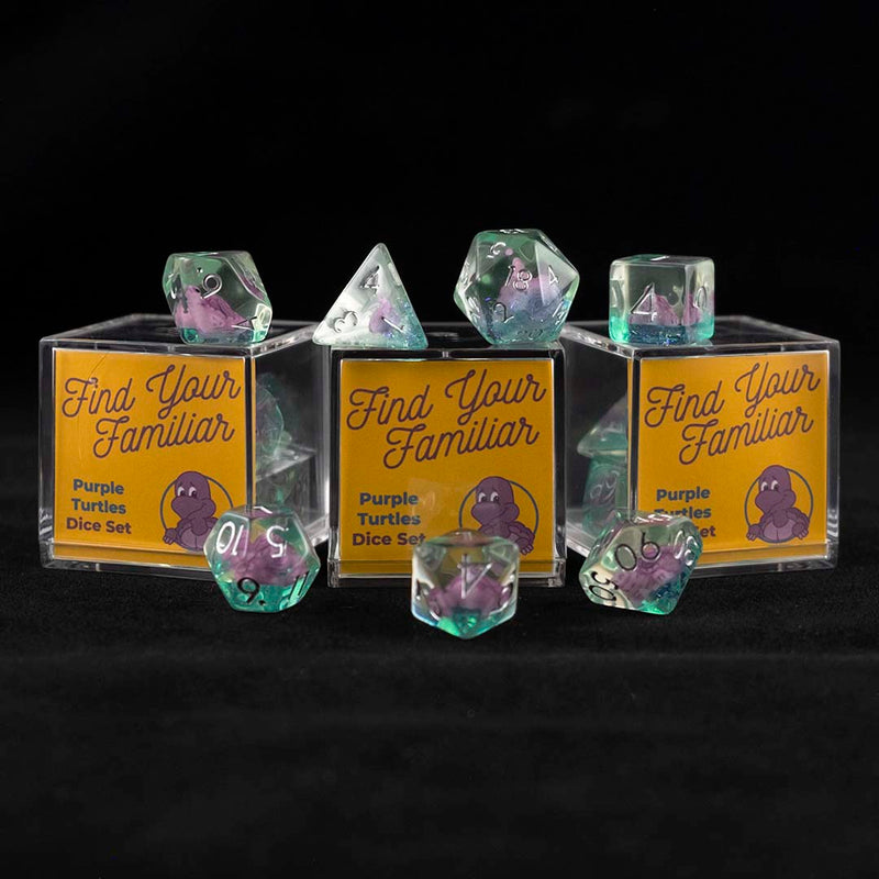 A set of clear green polyhedral dice with purple turtle inclusions sitting on top and around a three small acrylic boxes with the words "Find Your Familiar" and "Purple Turtles Dice Set" on a black background.