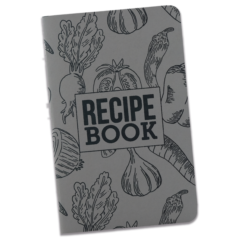 A large recipe notebook with a gray cover and black line illustrations of various vegetables with a rectangle with the words "Recipe Book" inside. The notebook is on a transparent background.