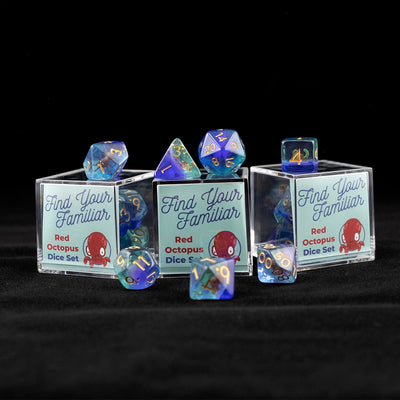 A set of clear green and blue polyhedral dice with red octopus inclusions sitting on top and around a three small acrylic boxes with the words "Find Your Familiar" and "Red Octopus Dice Set" on a black background.