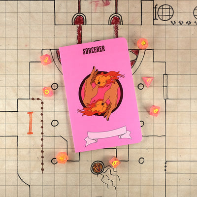 The front cover of a large sorcerer notebook with a light pink cover and an illustration of two hands with fireballs. The notebook sits on a grid map surrounded by dice.