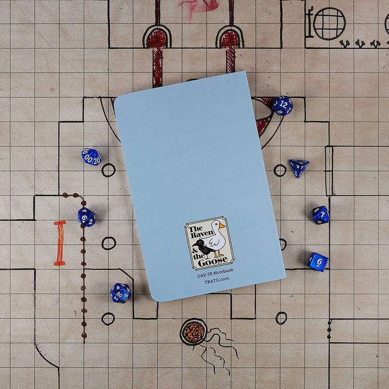 The light blue back cover of the wizard notebook with "The Raven and the Goose" logo on the bottom. The notebook sits on a grid map surrounded by dice.