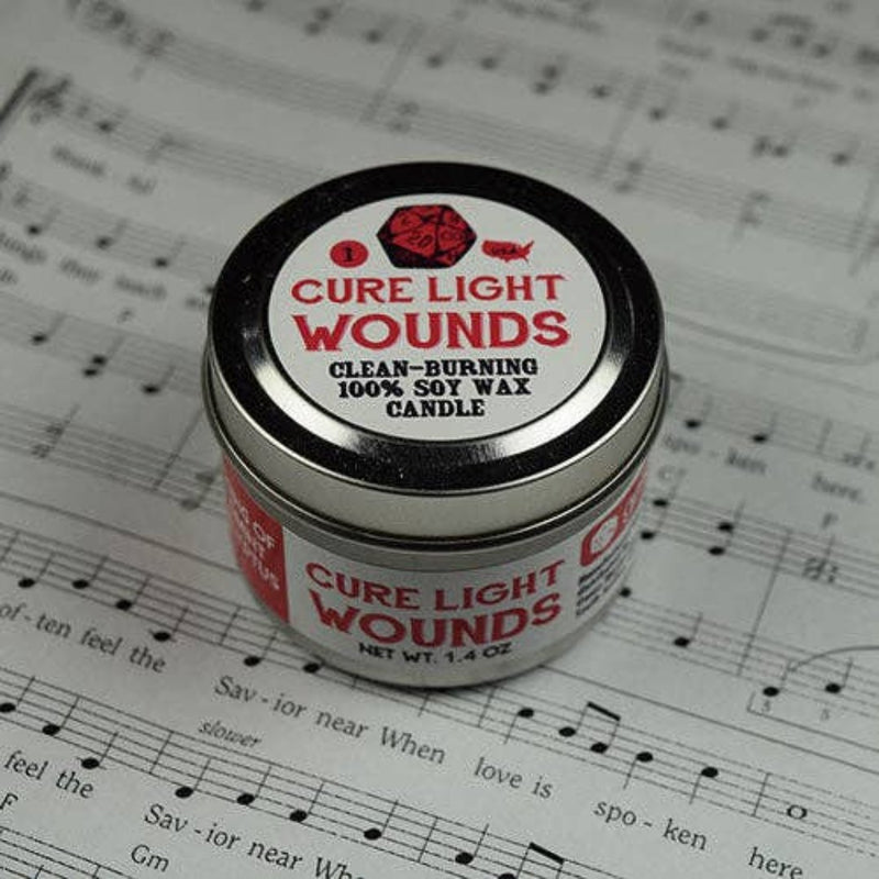 A small candle tin with the words "Cure Light Wounds" on the top and side sitting on a sheet of music.